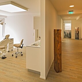 Moderne, helle Zahnarztpraxis mit Behandlungsraum, Zahnarztstuhl und Empfangsbereich.