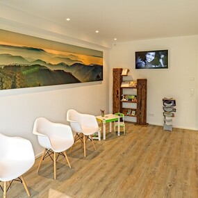 Modernes Wartezimmer mit weißen Stühlen, Holzfußboden und Wandbild einer Berglandschaft.