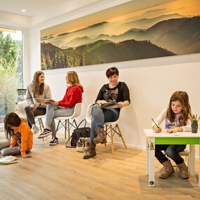 Heller Wartebereich mit Kindern und Erwachsenen, die lesen und malen, freundliche Atmosphäre.